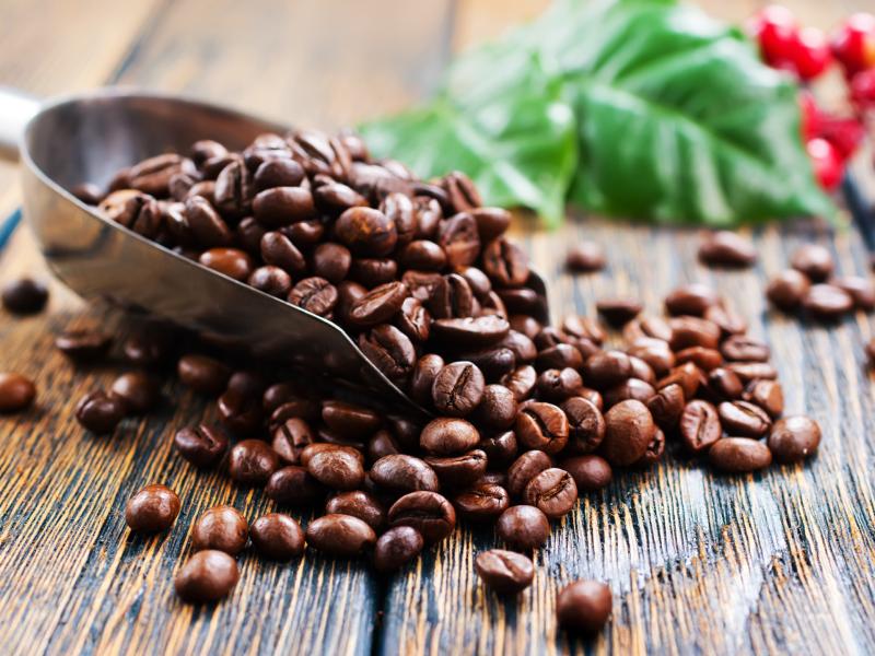 En håndfuld ristede kaffebønner i en lille skovl på et plankebord.